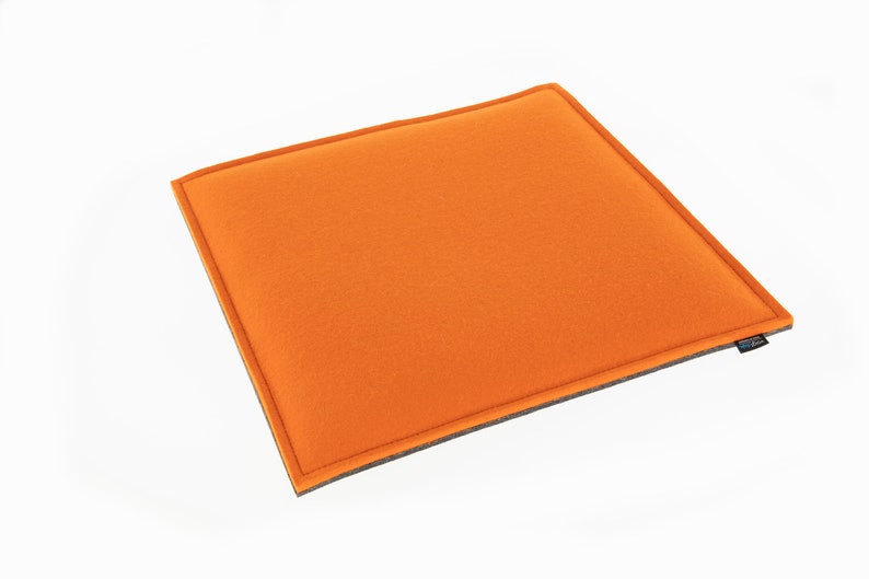 Op de afbeelding: Oranje gevoerd kussen met een grijze rand. Het kussen is rechthoekig en heeft een zachte, pluche textuur.