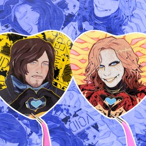 Op de afbeelding: Twee hartvormige fan art stickers. Eén toont een man met bruin haar en een blauw hart, de andere een persoon met rood haar en een blauw hart. Beide staan op een gele achtergrond met het woord "VOID".