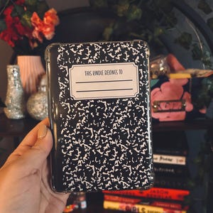 K&ouml;nnte beinhalten: Eine transparente Handyh&uuml;lle mit einem schwarz-wei&szlig;en Notizbuchmuster. Die H&uuml;lle tr&auml;gt den Text "THIS KINDLE BELONGS TO" mit einem leeren Feld zur Personalisierung. Die H&uuml;lle wird in einer Hand gehalten.