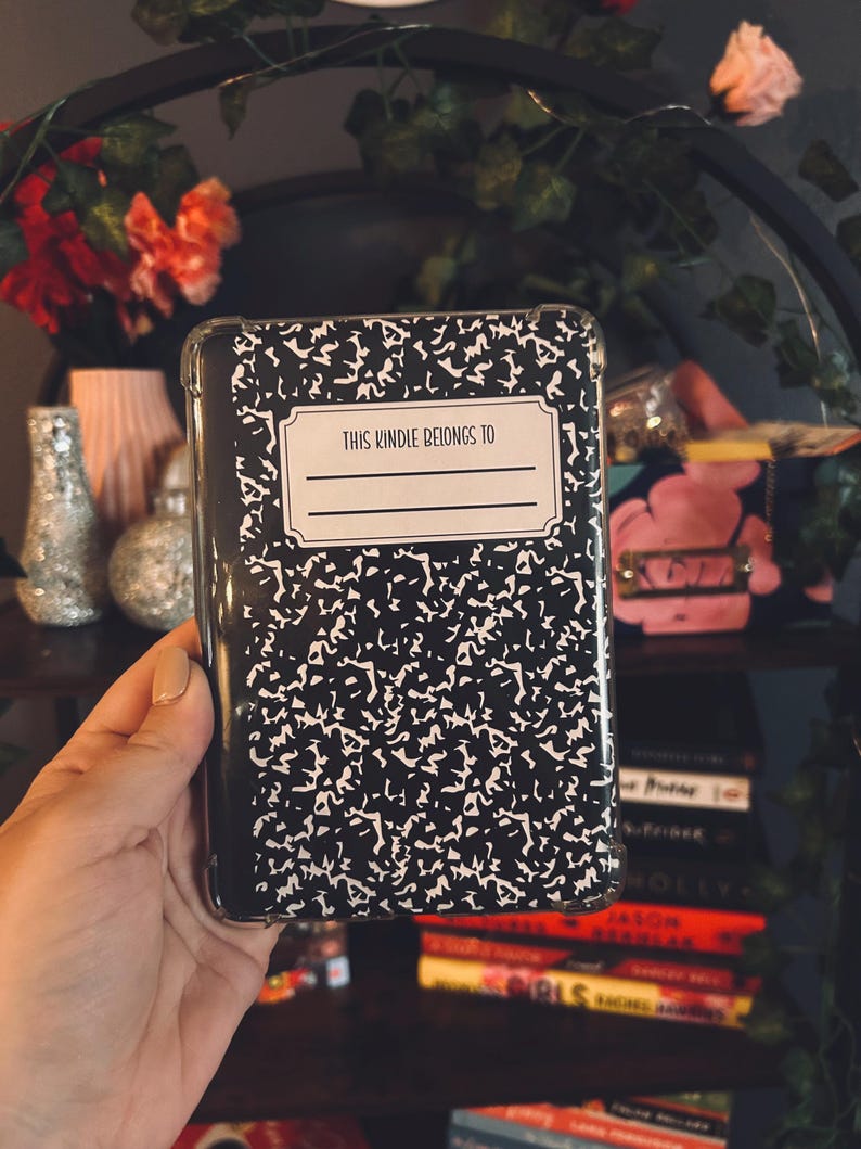 K&ouml;nnte beinhalten: Eine transparente Handyh&uuml;lle mit einem schwarz-wei&szlig;en Notizbuchmuster. Die H&uuml;lle tr&auml;gt den Text "THIS KINDLE BELONGS TO" mit einem leeren Feld zur Personalisierung. Die H&uuml;lle wird in einer Hand gehalten.