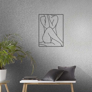 May include: A black and white line drawing of a person sitting with their arms crossed, framed in a black frame. The artwork is hanging on a gray textured wall.
