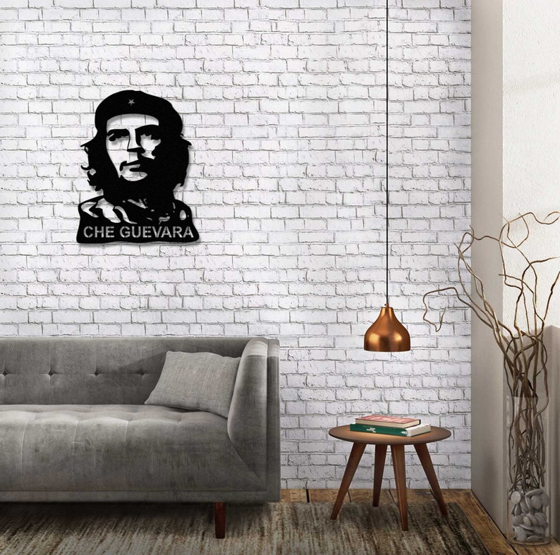 May include: Black and white metal wall art featuring a portrait of Che Guevara with the text "CHE GUEVARA" below. The art is displayed on a white brick wall above a gray couch and a wooden side table.