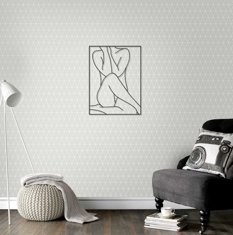 May include: A black and white line drawing of a person sitting with their legs crossed, framed in a black frame. The frame is hanging on a gray wall with a geometric pattern.