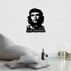 May include: Black and white silhouette wall art of Che Guevara, a famous revolutionary, with the text "CHE GUEVARA" below the image. The art is displayed on a white wall with a beanbag chair and two decorative fire pits in the foreground.