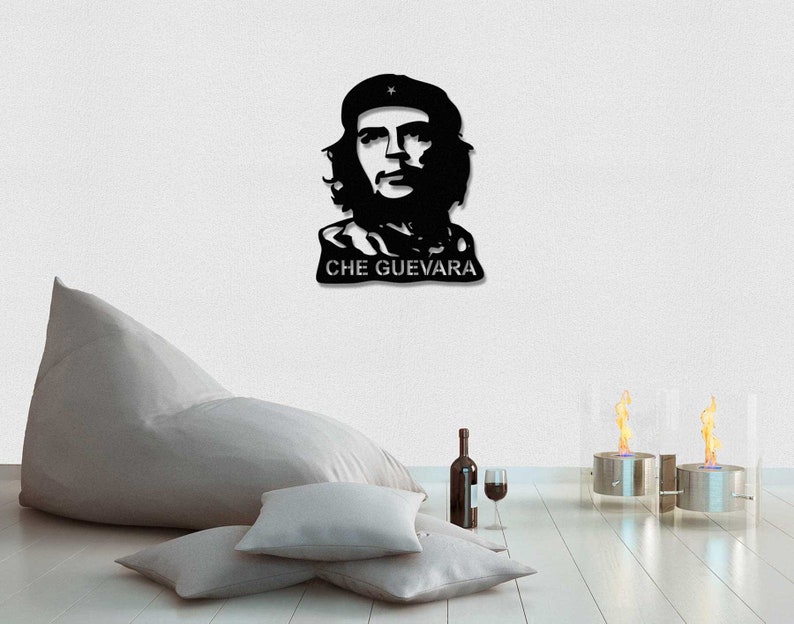 May include: Black and white silhouette wall art of Che Guevara, a famous revolutionary, with the text "CHE GUEVARA" below the image. The art is displayed on a white wall with a beanbag chair and two decorative fire pits in the foreground.