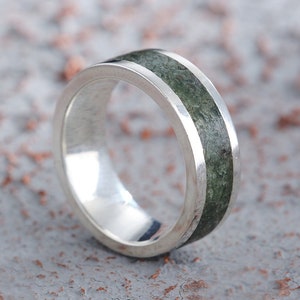 Könnte beinhalten: Ein silberner Ring mit einem grünen Steineinlege. Der Ring liegt auf einer strukturierten grauen Oberfläche.