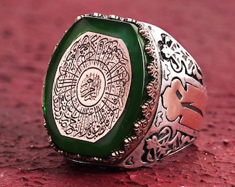May include: A silver ring with a green stone featuring Arabic calligraphy. The ring has intricate details and a decorative design.