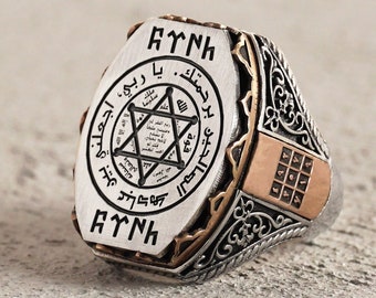 May include: A silver ring with a black and gold design. The ring features a star of David with Arabic script and the word "AYTNK" on the top and bottom of the ring.