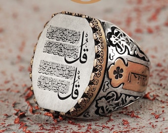 May include: A silver ring with intricate floral designs and a large oval-shaped center piece featuring Arabic calligraphy. The ring has a gold band and accents.