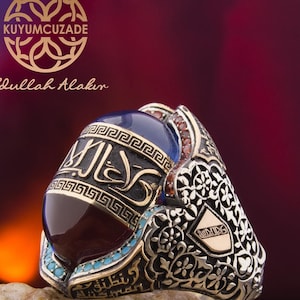 Può includere: Un anello d'argento con una grande pietra preziosa blu e rossa incastonata in una montatura d'argento dettagliata. L'anello presenta intricati motivi floreali e calligrafia araba.