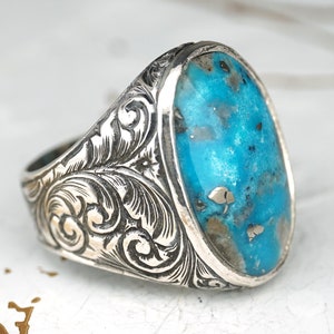 May include: A silver ring with an oval turquoise stone set in a detailed, engraved band.