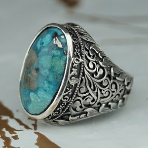 May include: A silver ring with an oval turquoise stone set in a filigree design.