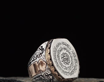 May include: A silver ring with a hexagonal face featuring intricate Arabic calligraphy in black. The ring has a gold band with a decorative design.