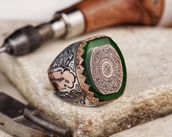 May include: A silver ring with intricate engravings and a large green stone set in the centre. The stone features Arabic calligraphy.