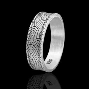 May include: A silver ring with a repeating wave pattern etched around the band. The ring is set against a black background, with a reflection visible below. The ring is marked with "925".