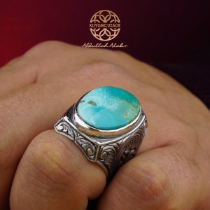 May include: A silver ring with a large turquoise gemstone set in a detailed, ornate design. The ring is on a person's finger.