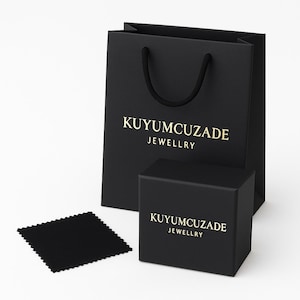 May include: A black gift bag, box, and cleaning cloth set. The bag and box feature gold text that reads "KUYUMCUZADE JEWELLRY". The bag has a black rope handle. The cleaning cloth is square and black.