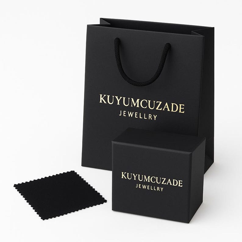 May include: A black gift bag, box, and cleaning cloth set. The bag and box feature gold text that reads "KUYUMCUZADE JEWELLRY". The bag has a black rope handle. The cleaning cloth is square and black.