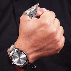 May include: A silver watch with a white face and black numbers on a black leather band. The watch is on a person's wrist, and the person is wearing a black shirt.