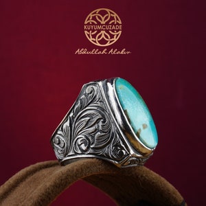 May include: A silver ring with an oval turquoise stone set in a detailed floral design. The ring is on a brown velvet surface.