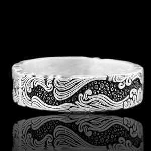 May include: A silver ring with an engraved wave pattern. The ring's design features flowing lines and dotted details, creating a textured appearance. The ring is displayed against a black background, with its reflection visible.