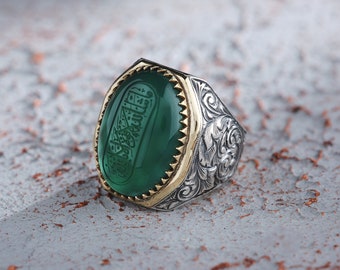 May include: A silver ring featuring a green stone set within a gold bezel. The stone is engraved with Arabic script. The ring band is adorned with floral patterns.