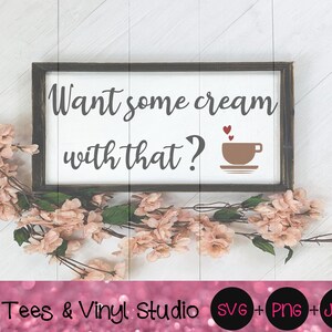 Puede incluir: Un cartel blanco con texto negro que dice "Want some cream with that?" y una taza de café marrón con corazones rojos encima. El cartel está enmarcado en un marco de madera marrón oscuro. El cartel está sobre una superficie de madera blanca con flores rosas.