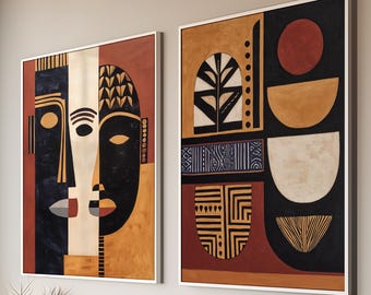 Puede incluir: Dos obras de arte abstractas enmarcadas con bordes blancos. Una presenta un diseño de rostro en negro, blanco y naranja. La otra tiene formas geométricas en negro, naranja y rojo. La obra de arte se exhibe sobre un mueble de madera clara.
