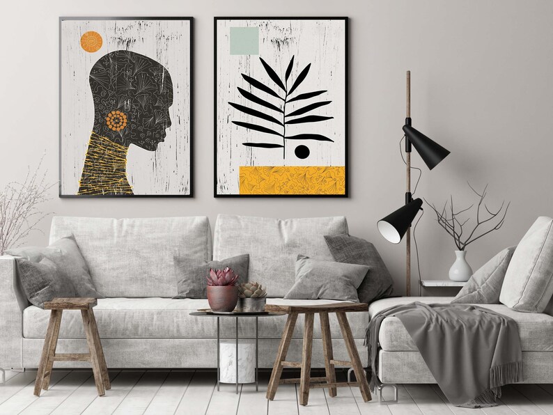 May include: Two framed abstract art prints on a white wall above a gray couch. The print on the left features a black silhouette of a person's head with a yellow and orange geometric pattern. The print on the right features a black silhouette of a leaf with a yellow and orange geometric pattern.