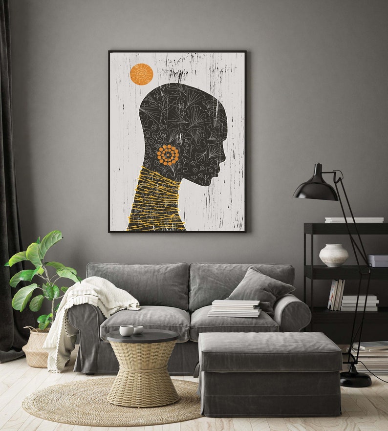 May include: A black and white illustration of a person's head with a yellow sun and black and white floral patterns. The illustration is framed and hanging on a gray wall above a gray couch.