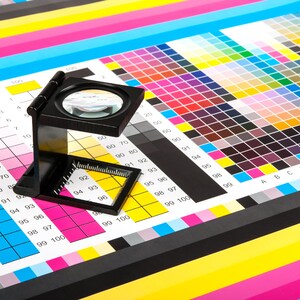 Pu&ograve; includere: Una lente d'ingrandimento &egrave; posizionata su una cartella colori con quadrati numerati. La cartella viene utilizzata per abbinare i colori per la stampa.