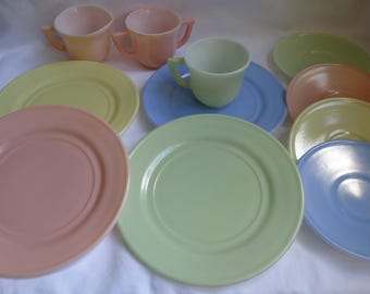 May include: A collection of pastel-colored vintage dishware, including plates, saucers, and teacups. The set features shades of pink, yellow, green, and blue. The teacups have small handles. The plates and saucers are round.