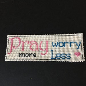 May include: White cross-stitch embroidery with pink and blue thread. The embroidery says "Pray More Worry Less" with a pink heart.