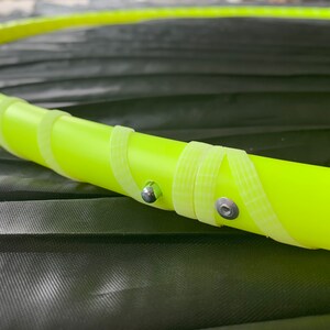 May include: Close-up of a yellow plastic hula hoop with silver metal accents. The hoop is wrapped with white tape.