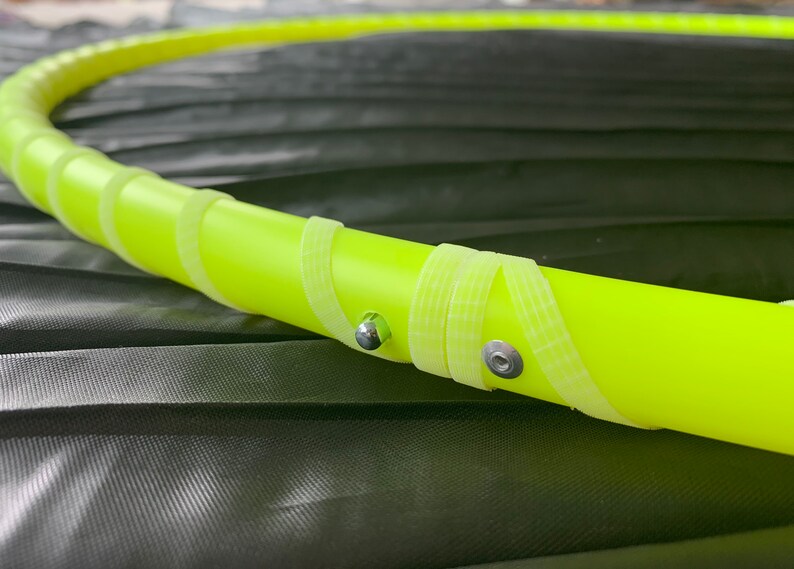 May include: Close-up of a yellow plastic hula hoop with silver metal accents. The hoop is wrapped with white tape.