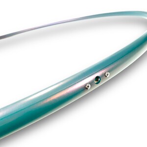 Puede incluir: Primer plano de un aro de color turquesa con tres tornillos plateados. El aro est&aacute; hecho de un material liso y brillante.