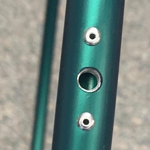 Puede incluir: Primer plano de un tubo met&aacute;lico verde con tres ojales plateados. Los ojales est&aacute;n espaciados uniformemente a lo largo del tubo.