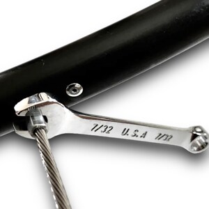 Puede incluir: Una llave inglesa plateada con el texto "7/32 U.S.A 7/32" se utiliza para apretar un cable conectado a un objeto de metal negro.