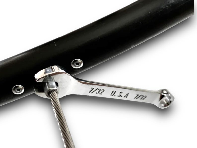 Puede incluir: Una llave inglesa plateada con el texto "7/32 U.S.A 7/32" se utiliza para apretar un cable conectado a un objeto de metal negro.