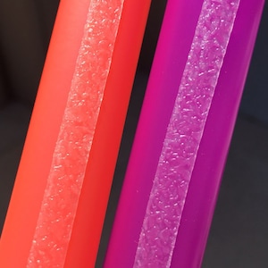 May include: Close-up of two colorful straws. One is a vibrant red, and the other is a deep purple. Each straw has a textured, translucent strip running down its length. The background is a dark gray.