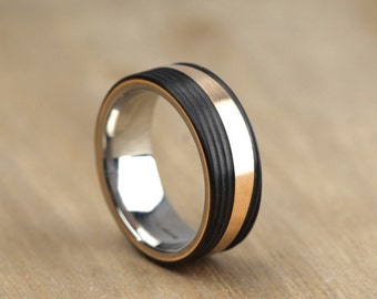 May include: A black and silver ring with a gold band. The ring has a textured black band with a thin gold band around it.
