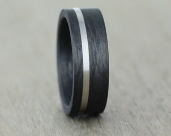May include: A black carbon fiber ring with a silver inlay. The ring is about 8mm wide and has a polished finish.