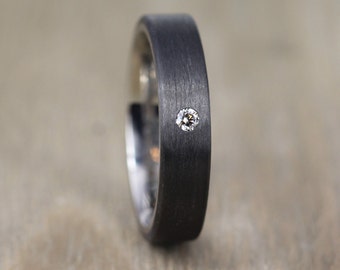 May include: A black brushed metal ring with a single small diamond set in the band.