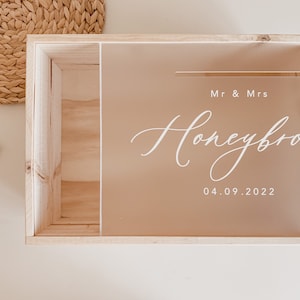 Puede incluir: Una caja de madera con una tapa de acr&iacute;lico transparente. La tapa tiene el texto "Mr & Mrs Honeymoon 04.09.2022" escrito en blanco.