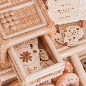 May include: A wooden play set with a drawer containing wooden coins and a paper bill with a daisy design. The set includes a menu board with drink options and felt donuts.
