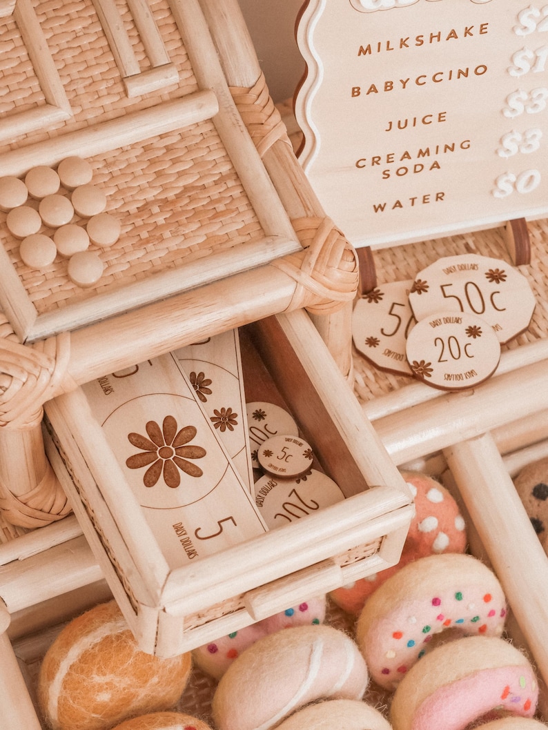 May include: A wooden play set with a drawer containing wooden coins and a paper bill with a daisy design. The set includes a menu board with drink options and felt donuts.
