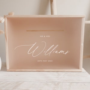 Puede incluir: Una caja de madera con una tapa de color marr&oacute;n claro y un inserto de acr&iacute;lico transparente. El inserto tiene un fondo marr&oacute;n claro con el texto "MR & MRS Williams 20th MAY 2022" en blanco.