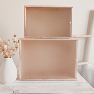 Puede incluir: Dos cajas de madera con frentes de vidrio apiladas una encima de la otra sobre una mesa de madera blanca. Las cajas est&aacute;n vac&iacute;as y tienen un acabado marr&oacute;n claro.