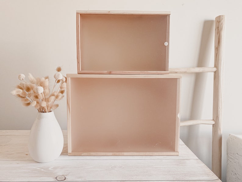 Puede incluir: Dos cajas de madera con frentes de vidrio apiladas una encima de la otra sobre una mesa de madera blanca. Las cajas est&aacute;n vac&iacute;as y tienen un acabado marr&oacute;n claro.