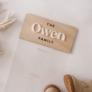 May include: A light wood growth chart featuring the text THE OWEN FAMILY in raised white and black lettering. The chart includes a clear vertical scale with markings from 190cm to 200cm, designed for tracking height measurements on a wall.